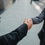 Close-up of two businessmen shaking hands outside, symbolizing partnership and agreement.